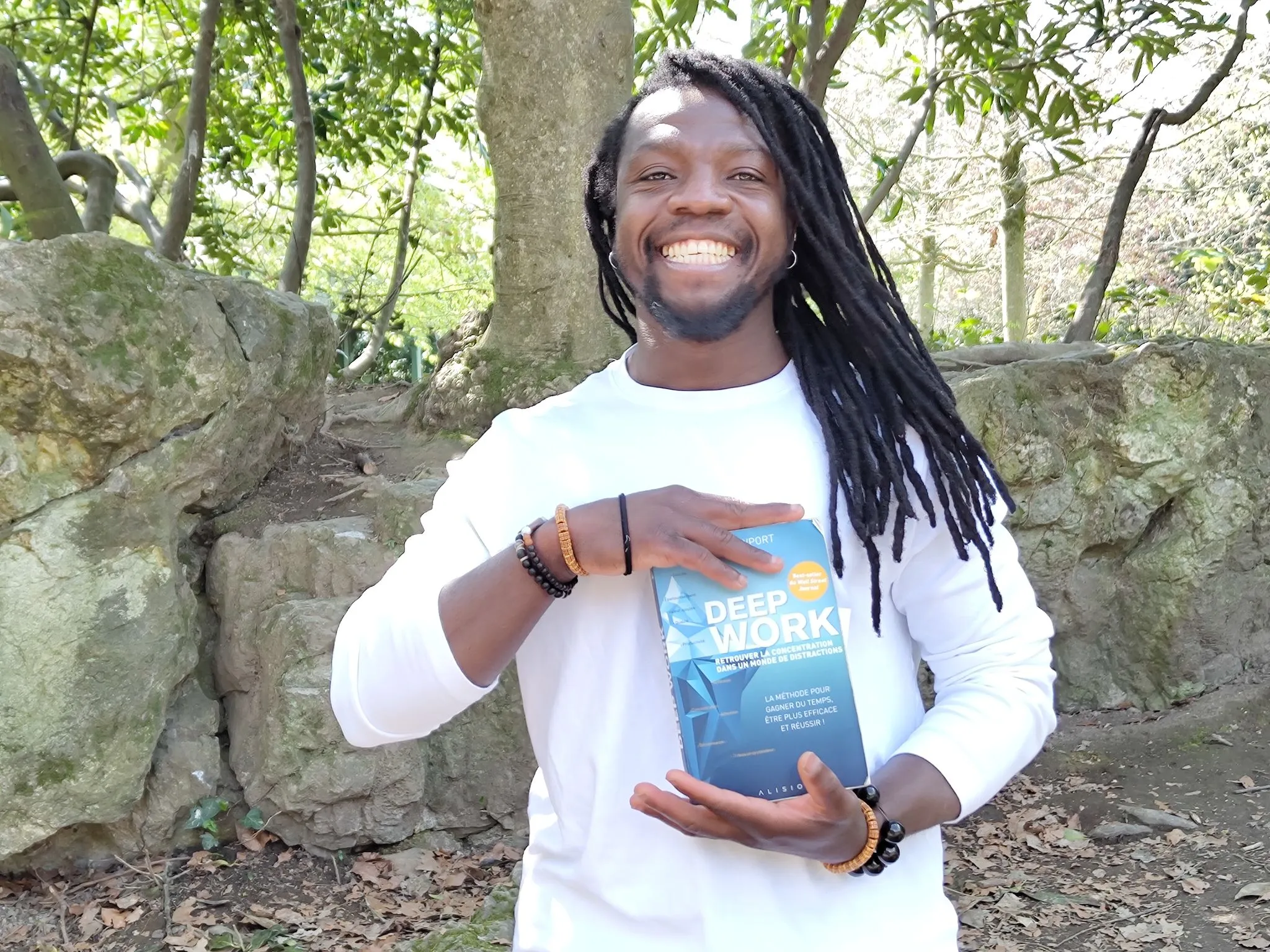 Photo de Yaya, fondateur de Soif de Connaissances, en train de sourire avec le livre de Cal Newport "Deepwork" lors d'un tournage vidéo.